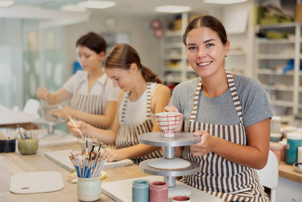 Women participating in a creative drop-in activity, painting pottery in a cosy studio setting, highlighting the accessibility and appeal of hands-on experiences.